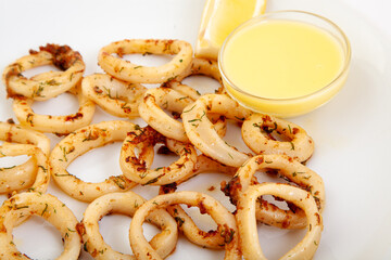 Gourmet fried calamari rings with herbs, served with a lemon dipping sauce. Delicious seafood appetizer or tapas dish on a white plate.