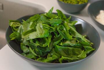  A close-up, elevated view of fresh, green basil leaves in a dark bowl indoors, conveying a sense of health and organic freshness.