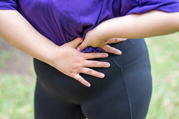 Overweight woman in a sporty outfit feeling a stomachache after practice exercise in a public park outdoors. Concept of a Healthy active lifestyle