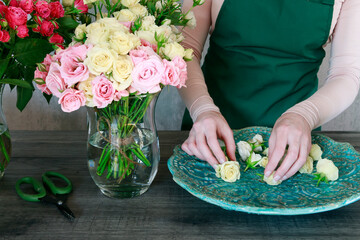 Woman (florist) is arranging a table decoration with tiny roses.