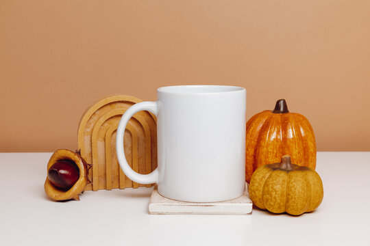 Ceramic mockup white cup on wooden coaster with pumpkin and autumn decorations. Mockup mug for design, logo or print, autumn, Thanksgiving theme