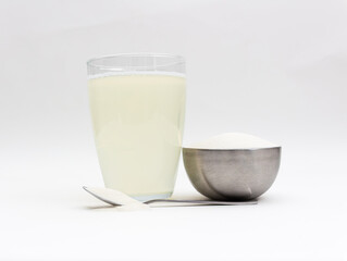 Spilled, dry collagen powder in metal container and spoon next to liquid, dissolved collagen in front of background. Version 10.