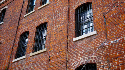 Obraz premium Rows of arched windows with black metal bars line a red brick building’s facade, evoking the secure, institutional atmosphere typical of prisons or detention centers.
