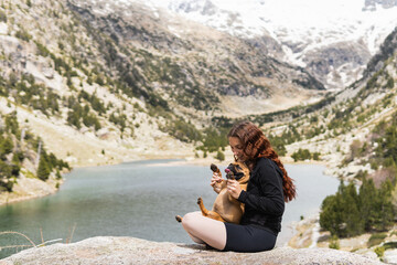 Young woman playing with french bulldog near to lake. Travel and adventure concept