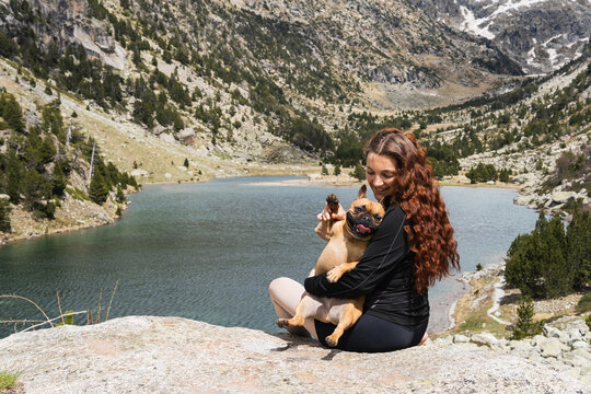 Dog saying hi to you. Young woman and french bulldog enjoying lake view in national park