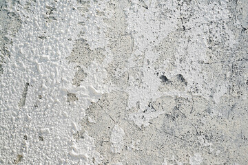 Closeup view of heavily textured white painted concrete wall. The surface is old and worn with peeling paint. Abstract background