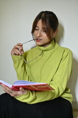 young woman reading a book. glasses in hands. white wall. time to read. enjoy with a book