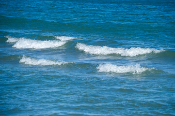 Obraz premium Gentle waves ripple across a deep blue ocean, crowned with soft white foam.
