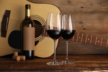 Acoustic guitar, bottle and glasses of red wine on wooden table