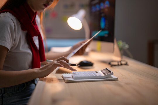 A woman is sitting at a desk with a calculator and a piece of paper