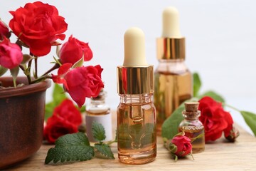 Bottles of essential oils, red roses and herbs on wooden table, closeup