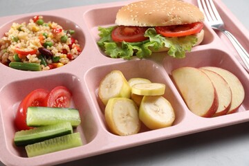 Plastic tray with tasty food and fork on grey table, closeup. School lunch
