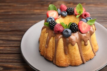Tasty Bundt cake with berries, chocolate and mint on wooden table, closeup