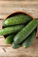 Fresh cucumbers in bowl on wooden table, top view
