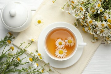 Tasty chamomile tea and flowers on white wooden table, flat lay