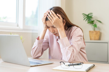 Stressed, exhausted asian young woman having migraine symptoms headache, bored sitting work long time, suffering from dizziness, holding head with hand office syndrome. Health care problem of worker.