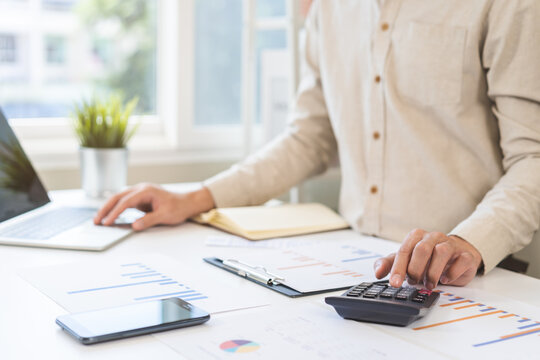 Account finance, asian young business man hand using calculator, laptop computer for calculate budget, cost and income of company from paperwork, plan spend money expenses, working on desk at home.
