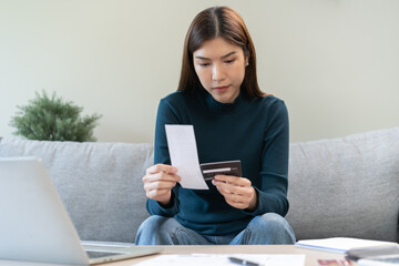 Fototapeta premium Stressed asian young business woman, employee calculate expenses of monthly, hand holding bills, receipt and credit card to payment on table at home. Financial, finance of banking concept.