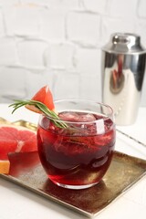 Tasty cocktail with grapefruit, ice cubes, rosemary and shaker on white table, closeup