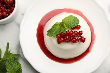 Delicious panna cotta with red currants, sauce and mint on white marble table, flat lay