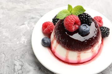 Tasty panna cotta with berries and jam on light grey table, closeup