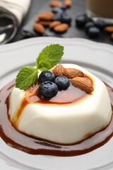 Tasty panna cotta with blueberries, almonds and sauce on table, closeup