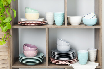 Shelving unit with different dishware, cups and floral decor near white wall indoors