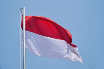 The Indonesian flag flies on a pole against a backdrop of bright blue sky.