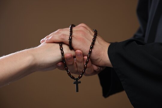 Priest and woman holding hands on brown background, closeup
