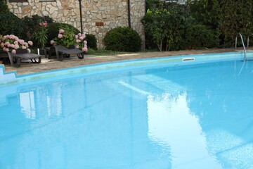 Outdoor swimming pool, sunbeds and green plants near hotel at luxury resort