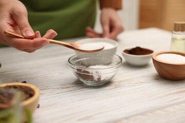 Making natural scrub. Woman adding sugar into bowl at white wooden table, closeup