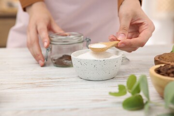 Making natural scrub. Woman adding sugar into jar at white wooden table, closeup