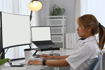 Side view of a focused female software engineer working with a computer and a laptop at workstation
