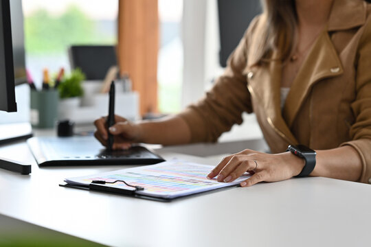Close-up of woman using stylus with a graphics tablet and examining a color guide during a design session