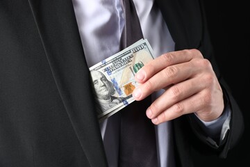 Man putting dollars in pocket on black background, closeup