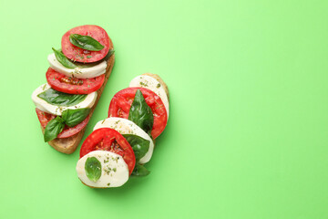 Delicious sandwiches with mozzarella cheese, tomatoes and basil on green background, flat lay. Space for text