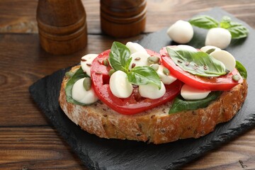 Delicious sandwich with mozzarella cheese, tomatoes and basil on wooden table, closeup