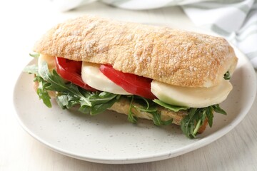 Delicious sandwich with mozzarella cheese, tomato and arugula on light wooden table, closeup