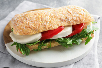 Delicious sandwich with mozzarella cheese, tomato and arugula on table, closeup