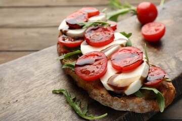Delicious sandwich with mozzarella cheese, balsamic sauce, tomatoes and arugula on wooden table, closeup. Space for text