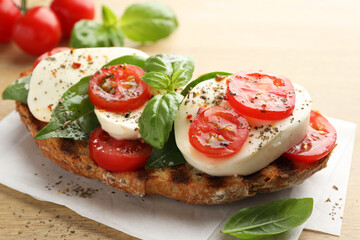 Delicious sandwich with mozzarella cheese, tomatoes and basil on wooden table, closeup