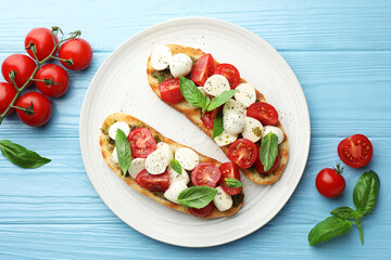 Delicious sandwiches with mozzarella cheese, tomatoes and basil on light blue wooden table, flat lay