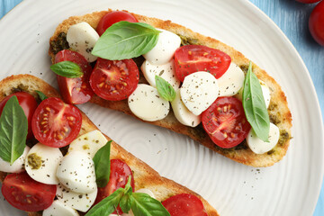Delicious sandwiches with mozzarella cheese, tomatoes and basil on light blue wooden table, flat lay