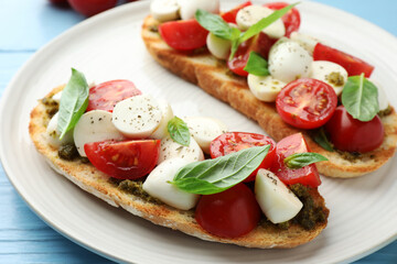 Delicious sandwiches with mozzarella cheese, tomatoes and basil on light blue wooden table, closeup