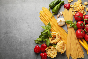 Different types of raw pasta and products on grey textured table, flat lay. Space for text