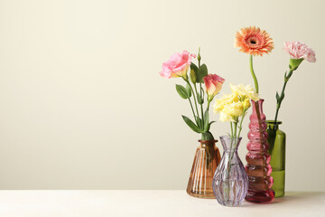 Different beautiful flowers in glass vases on white table against light grey background, space for text