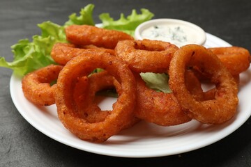 Fried squid rings served with sauce on black table, closeup