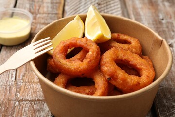 Fried squid rings, lemon and sauce on wooden table, closeup