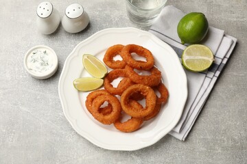 Fried squid rings, lime and sauce on grey table, flat lay