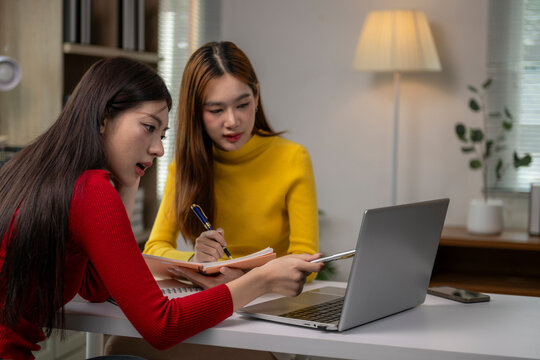 Two women are sitting at a table with a laptop open in front of them - Powered by Adobe